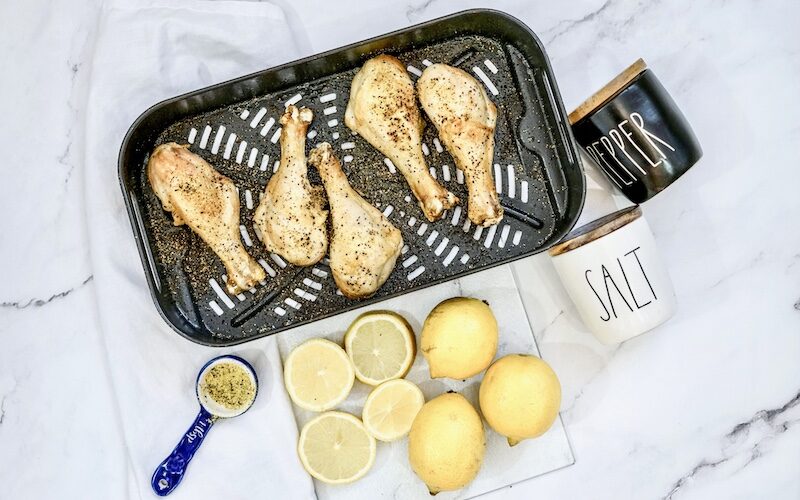 An image showing cooked lemon pepper chicken drumsticks in an air fryer basket