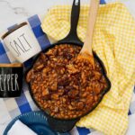A cast iron pan with baked beans and burnt ends next to a salt and pepper jar.