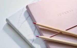 Two pencils and a pink journal about how to make money selling journals.