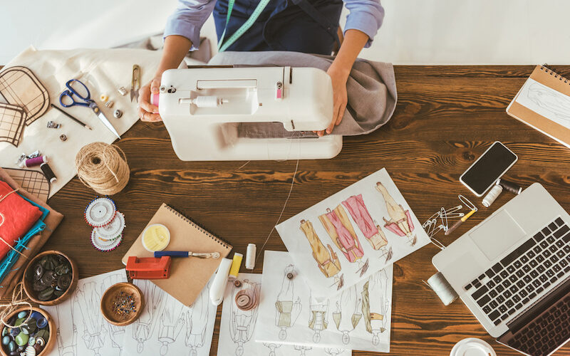 A person sitting at a desk with a sewing machine learning how to make money sewing.