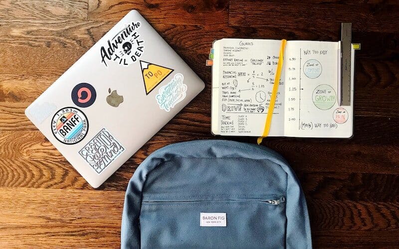 A laptop, backpack, and notebook on a wooden table.